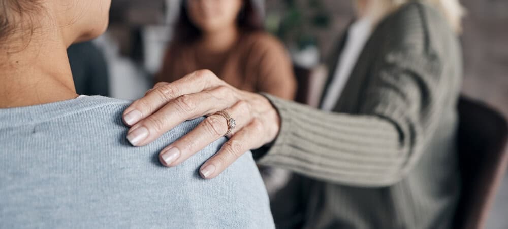 person puts hands on grieving person’s shoulder