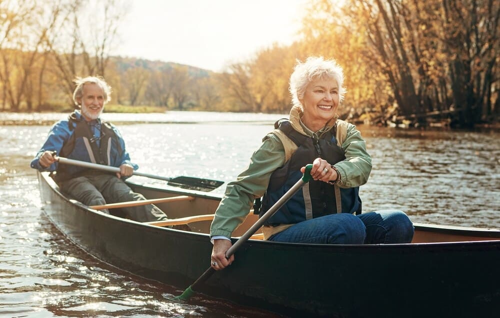 elderly couple kayaking down a river in Autumn.